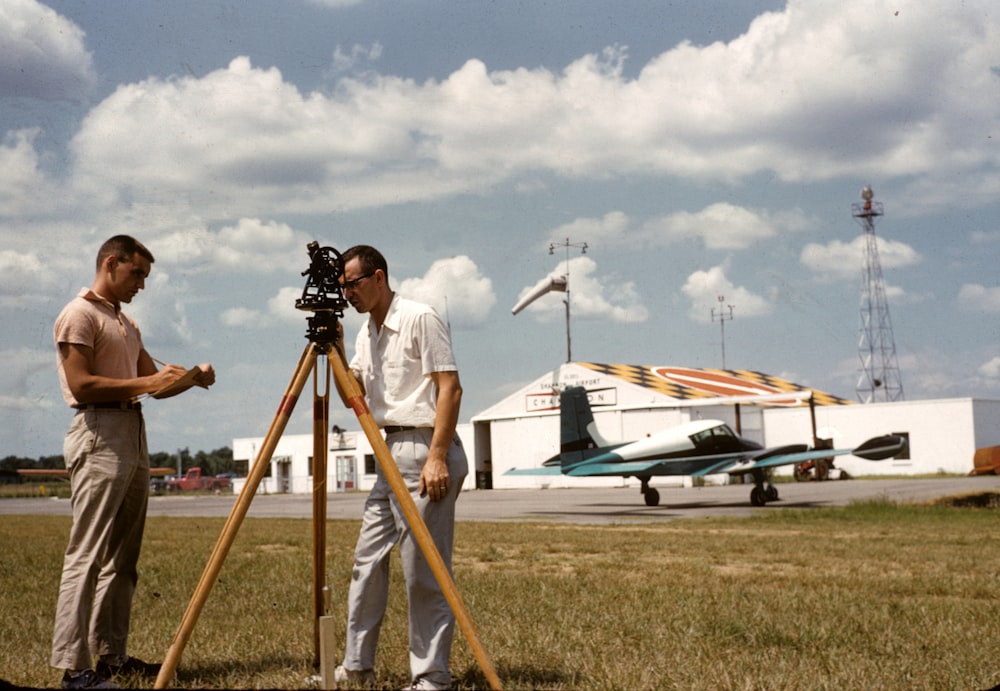 two men standing beside brown wooden tripod