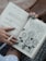 An open journal is held by a person with blue painted nails. The left page contains handwritten notes, including phrases of gratitude and tasks, dated Monday, 19.08.2019. The right page features artistic doodles of flowers labeled with positive traits like 'self love' and 'honesty', surrounded by encouraging words.