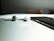A pair of wireless earphones and a smartphone rest on a reflective white surface, with subtle shadows and a blurred background.