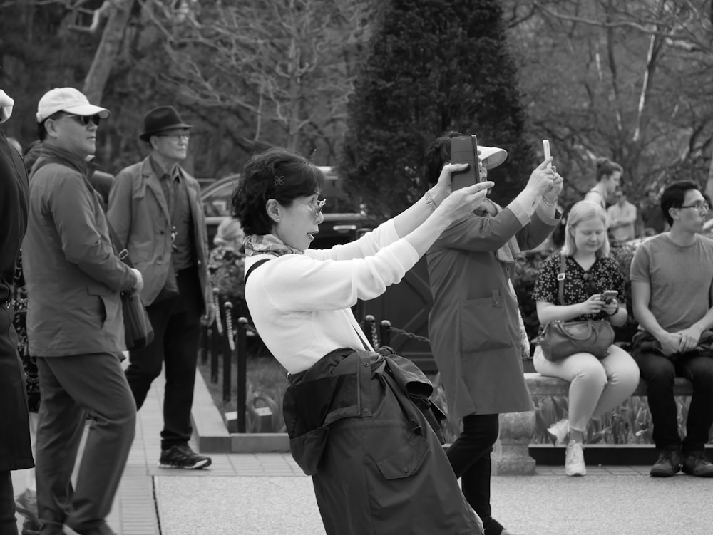 grayscale photo of woman wearing white blouse taking photo using smartphone