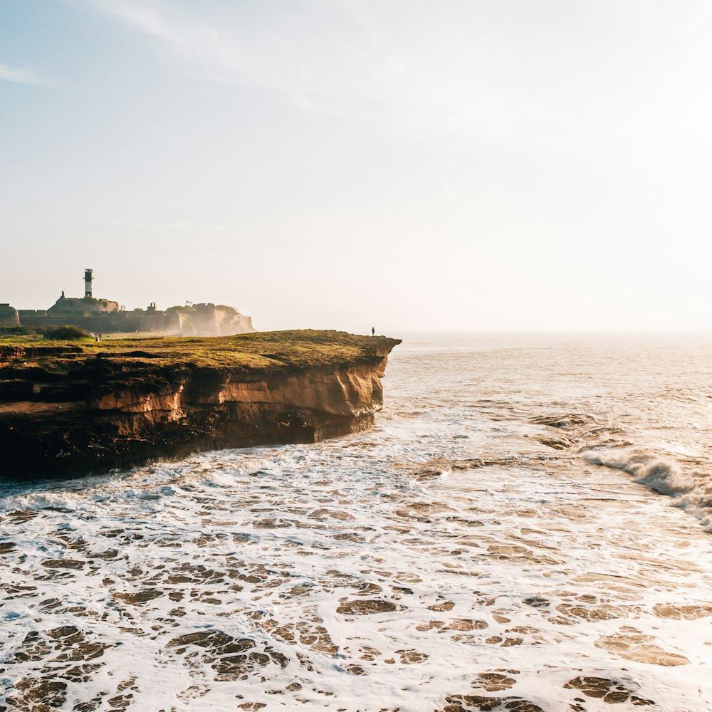 silhouette of person standing on top of mountain cliff facing on seashore during daytime