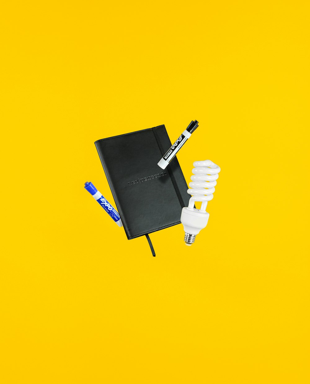 black and blue Expo markers near white CFL bulb and black hardbound book
