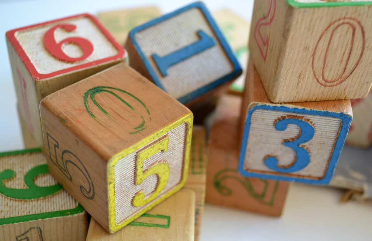 Natural wooden toy blocks with letters and numbers stacked loosely on a pale surface