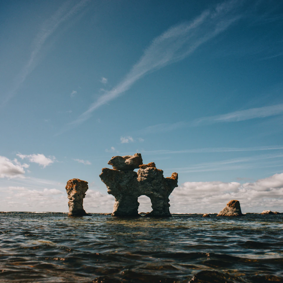 Three large, jagged rocks protrude from the water's surface in the clear blue sky