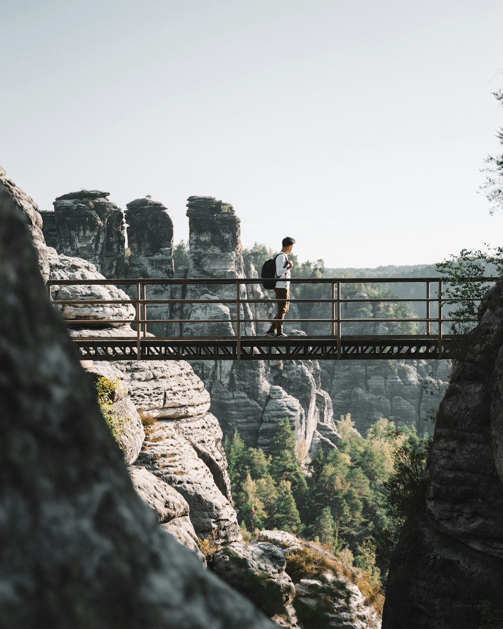 man wearing white shirt carrying backpack standing on bridge