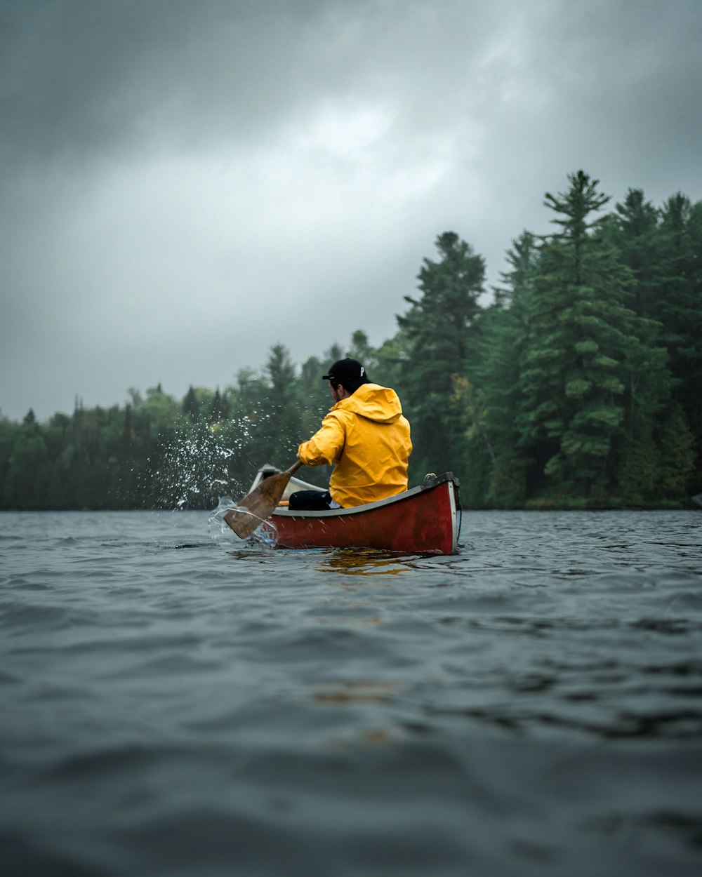 호수에서 빨간 카누를 타고 주황색 까마귀를 입은 남자