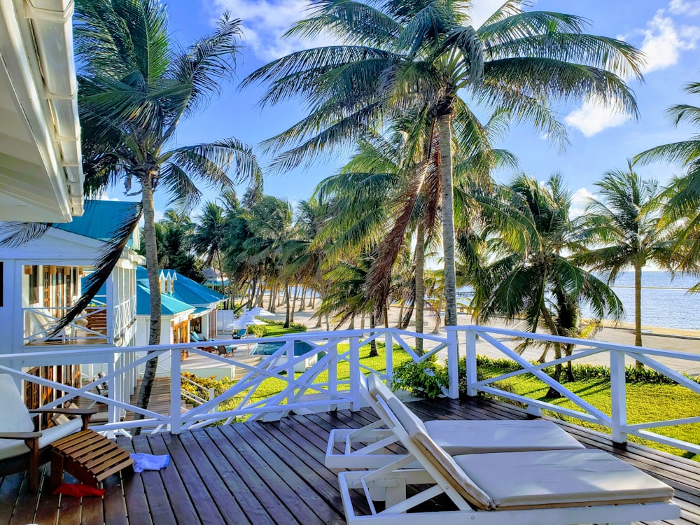 lounge chairs on wooden deck with railings near trees on the beach during day