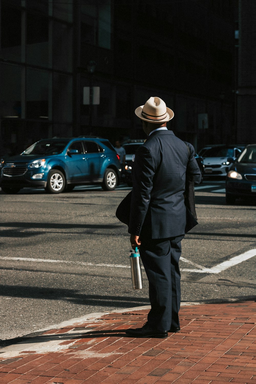 man wearing black suit standing on sidewalk while wearing beige fedora during daytime