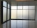 Large floor-to-ceiling glass windows are framed in dark metal, creating a modern and minimalistic design. The frosted glass provides a blurred view of the outside, allowing softened light to filter into the room. The floor is polished and reflects the light softly, adding to the clean and uncluttered aesthetic.