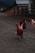 Several chickens are walking on a gravel path near a wooden fence with a rustic building nearby, set against a backdrop of rolling hills under a cloudy sky.