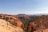 Vast landscape featuring striking orange and red rock formations, with pointed spires known as hoodoos. Dense green forestry spans the lower areas, contrasting with the natural stone structures, under a clear blue sky.