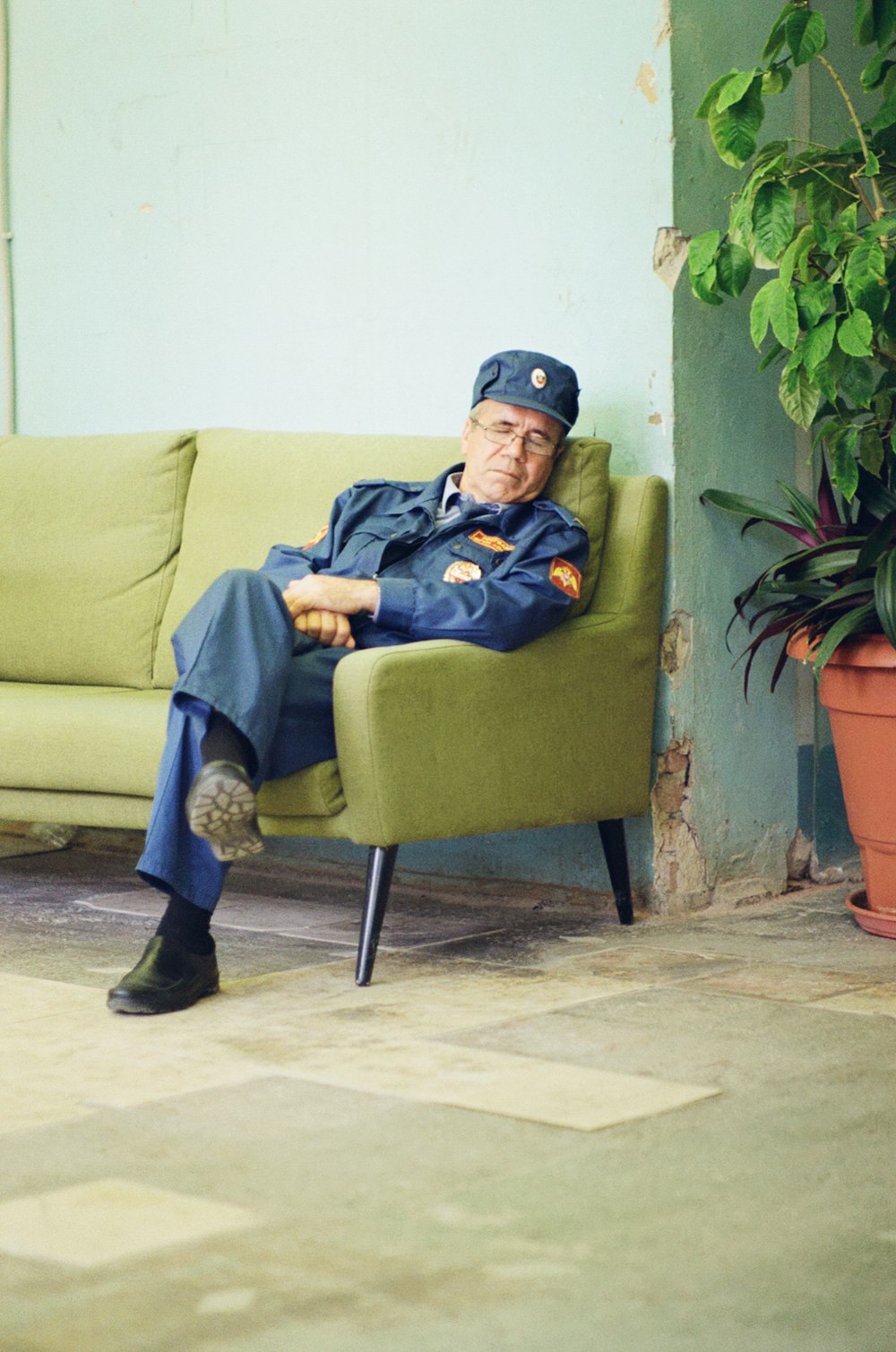 man wearing blue jacket sitting with crossed legs on green couch while sleeping