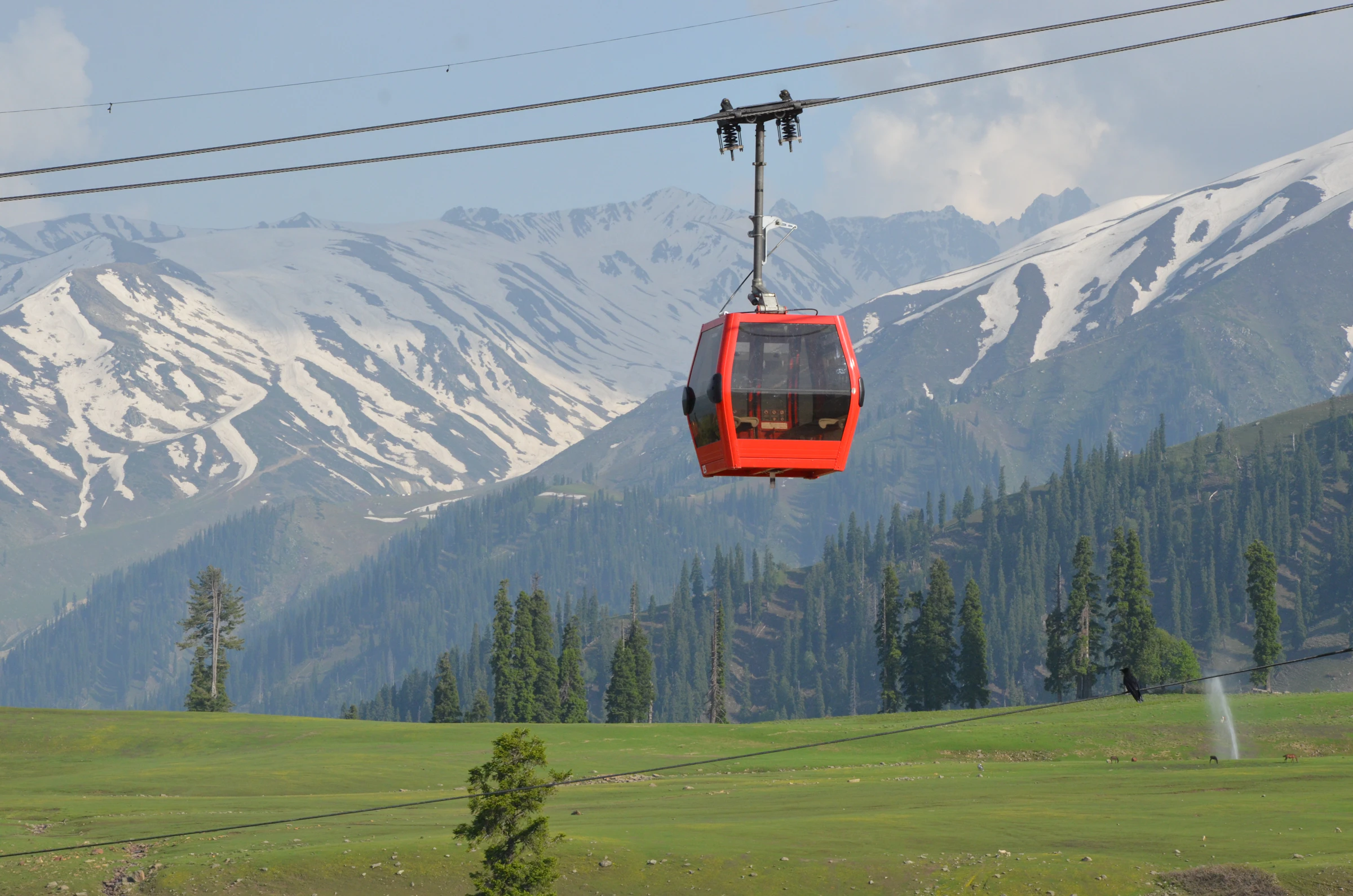 Red gondola cable car rising above snowy slopes, Gulmarg