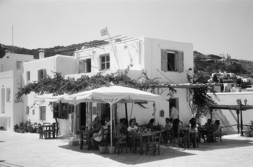 grayscale photo of people on tables near buildings