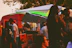 A colorful food truck with festival-goers enjoying meals near tents and vendor booths.