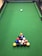 A green pool table with a neatly arranged triangular rack of colorful billiard balls positioned near one end. A single cue ball is placed further up the table, away from the rack.