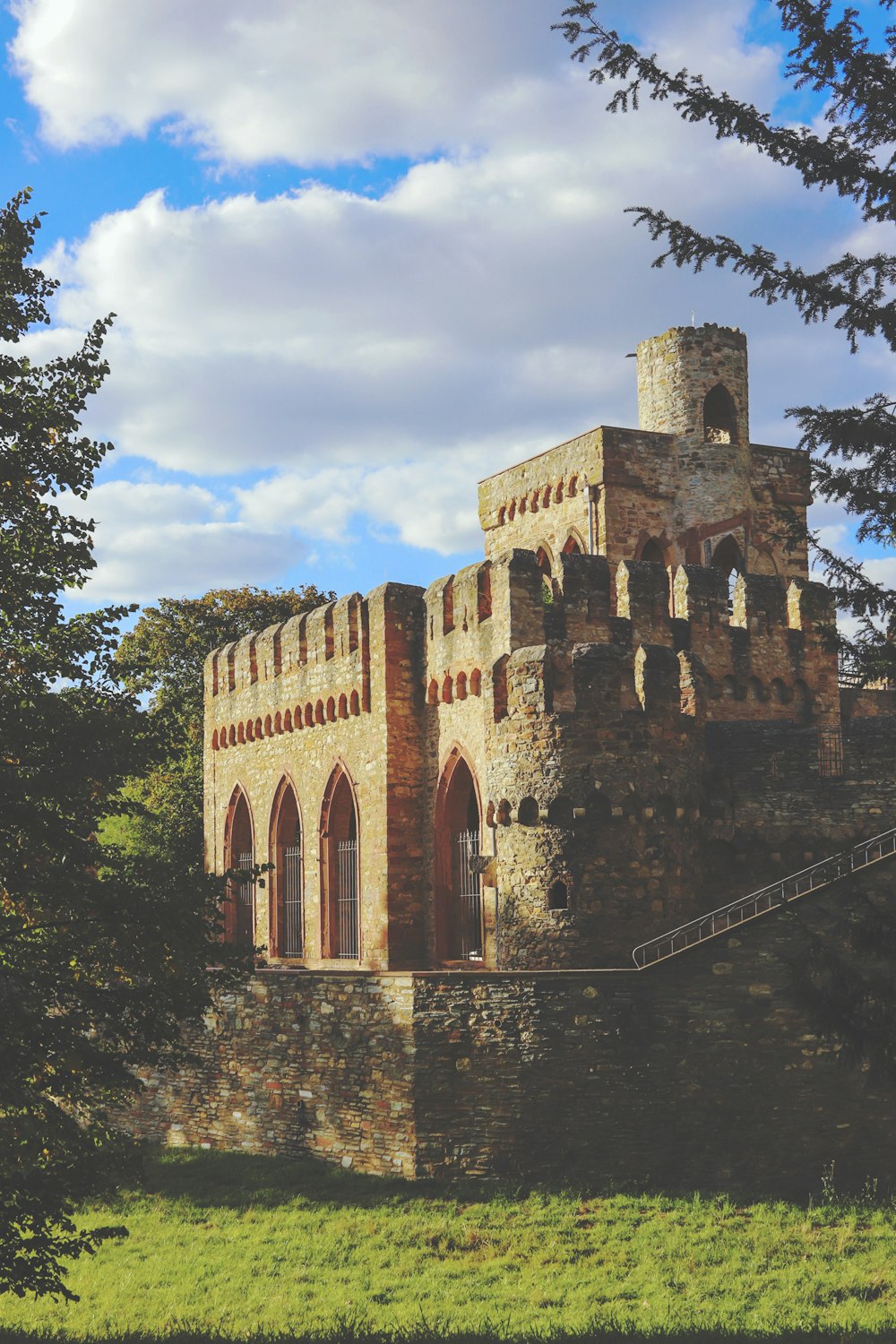 brown castle surrounded with tall and green trees under blue and white skies during daytime