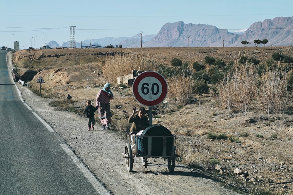 person pushing cart in front of walking woman and child at the side of the road during day