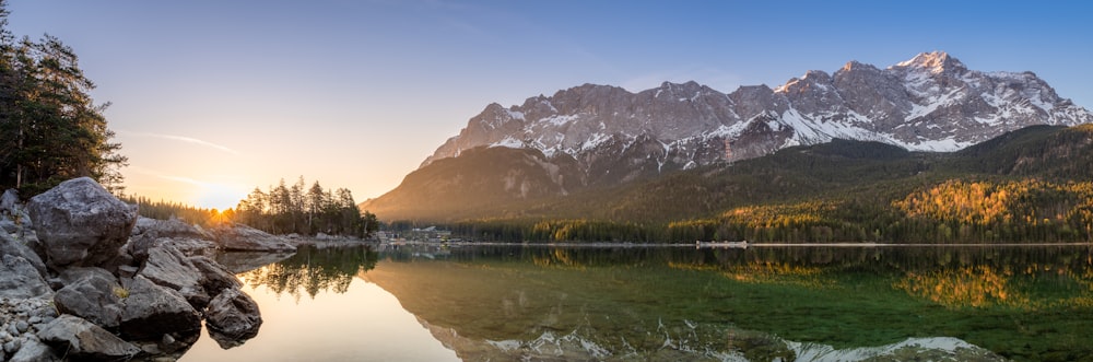 lake surrounded with tall and green trees viewing mountain during sunrise