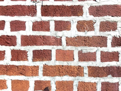 A close-up view of a brick wall with red bricks and gray mortar. The bricks are arranged in a staggered pattern typical of traditional masonry work.