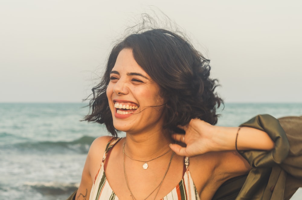 woman in white, brown, and black striped spaghetti strap top, laughing