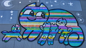 A group of smiling children and adults gathered around a colorful mural featuring playful cats.