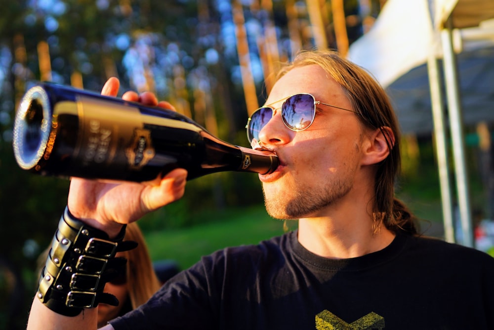 黒いクルーネックのTシャツを着た男が酒を飲む