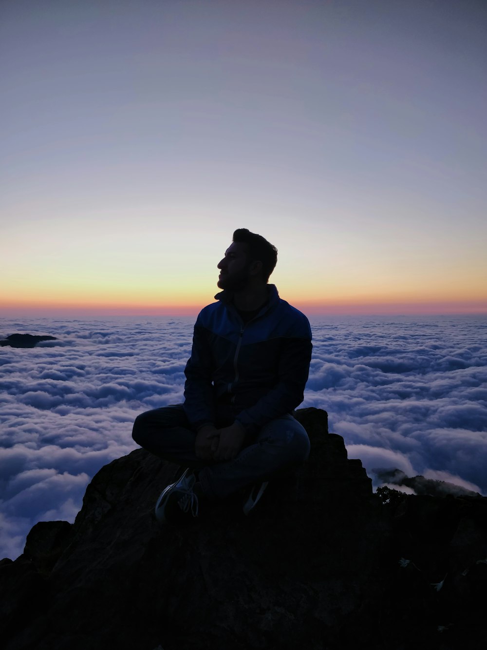 silhouette photo of man sitting on rock formation