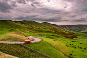 Road winding through lush green hills, framed by the perspective from inside a van window.