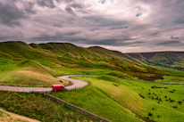 A panoramic shot of a winding mountain road with a van driving through lush green landscapes.