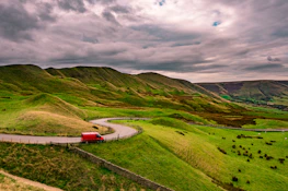 Road winding through lush green hills, framed by the perspective from inside a van window.