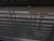 A reflective surface captures the pattern of shadows and a structural lattice above. In the background, a small object, possibly a crumpled paper or piece of trash, is situated on the floor. The shadows create a striped effect on the otherwise neutral ground, and the reflection presents layered dimensions.