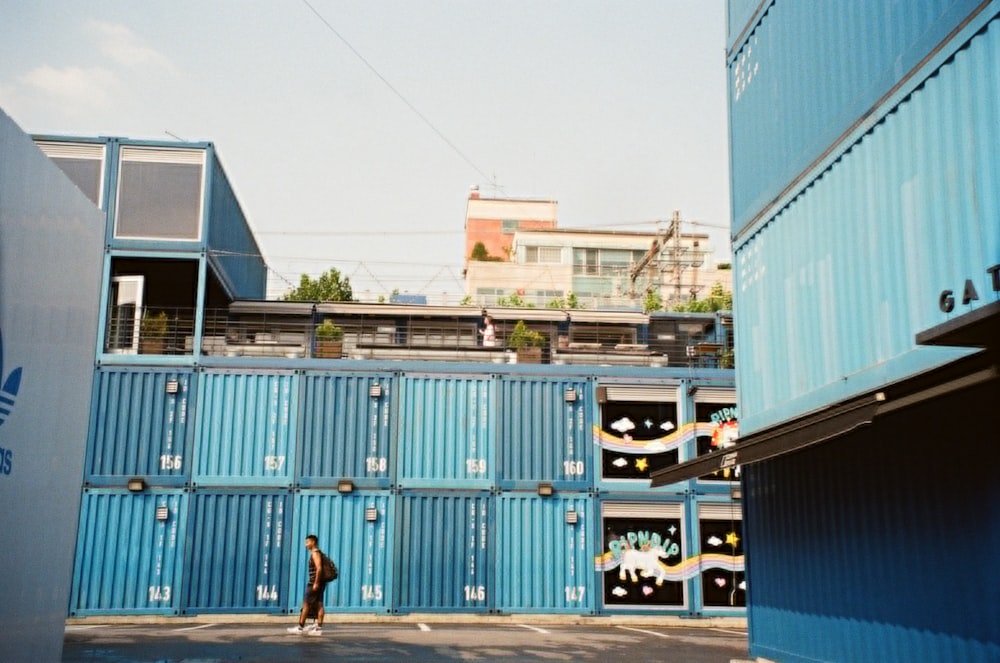 man walking beside blue cargo containers during daytime