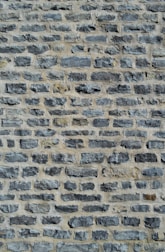 A close-up view of a stone wall featuring unevenly sized and shaped gray stones arranged in horizontal rows with a light mortar in between.