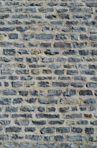 A close-up view of a stone wall featuring unevenly sized and shaped gray stones arranged in horizontal rows with a light mortar in between.