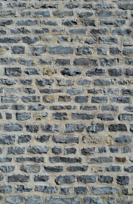 A close-up view of a stone wall featuring unevenly sized and shaped gray stones arranged in horizontal rows with a light mortar in between.