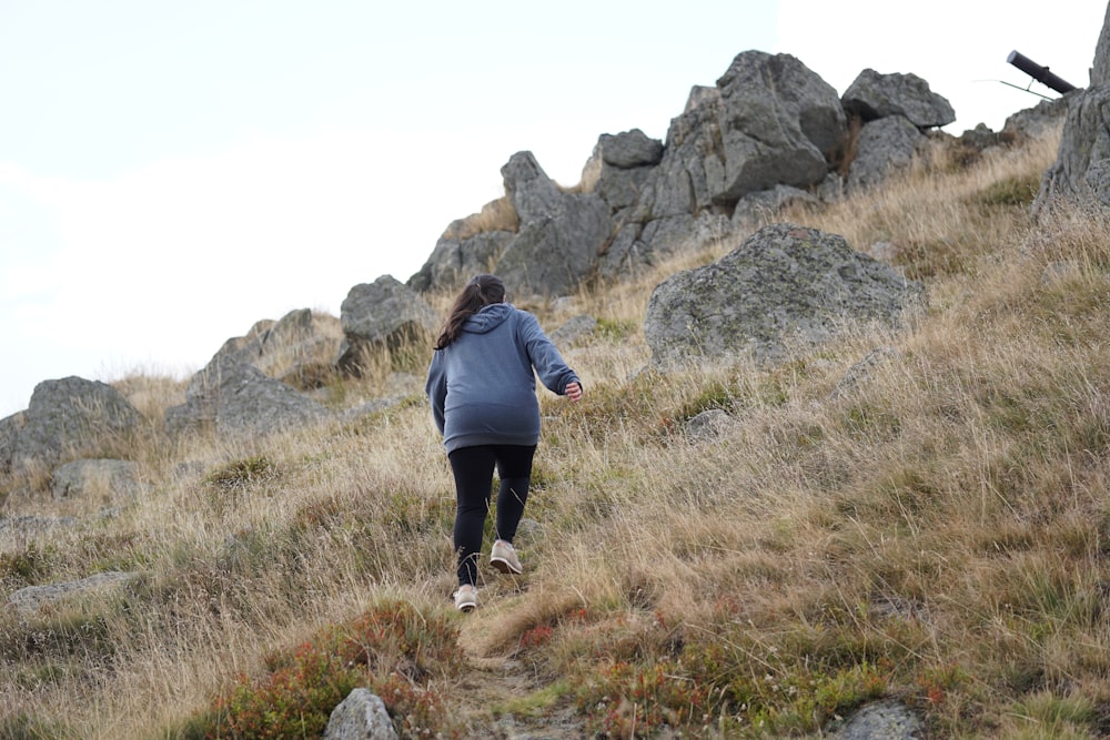 Frau in grauer Jacke klettert auf einen Berghang