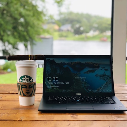 Rustic wooden table with an open laptop overlooking a coffee plantation at sunrise in the mountains.