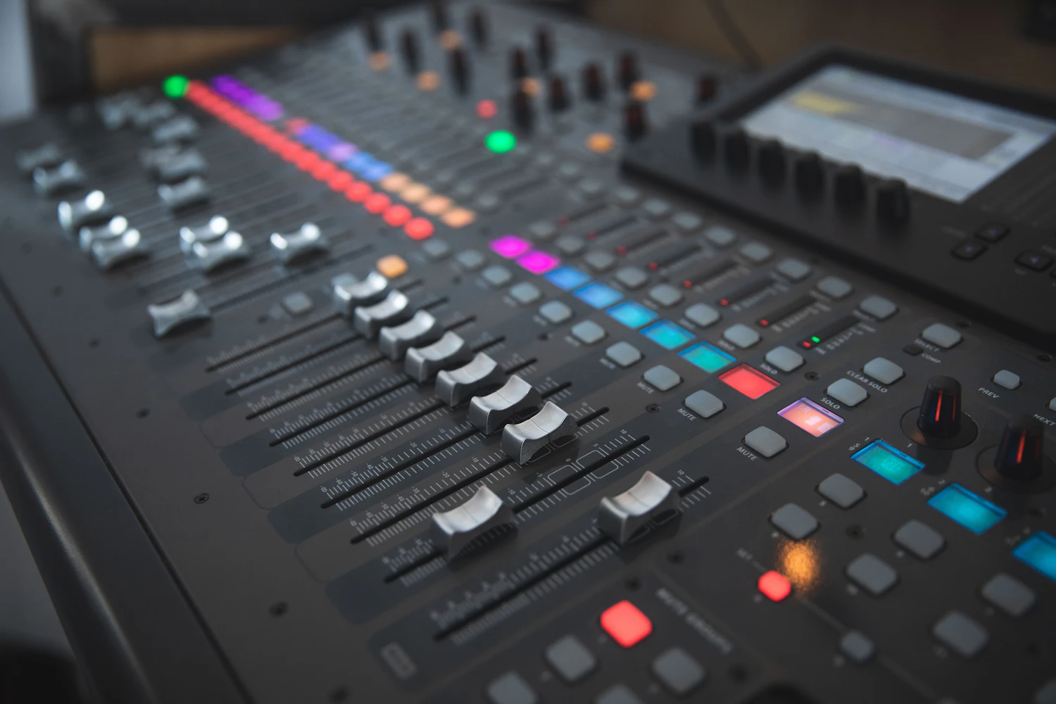 A hand resting on the faders of a lit mixing desk at the back of a dark room