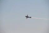 A sleek aerobatic plane twisting sharply against a clear blue sky.
