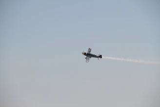 A sleek aerobatic plane performing a sharp roll against a clear blue sky.