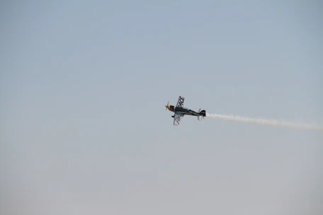 A sleek aerobatic plane performing a sharp roll against a clear blue sky.