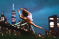 A dancer mid-leap on an urban rooftop with the city skyline softly blurred in the background.