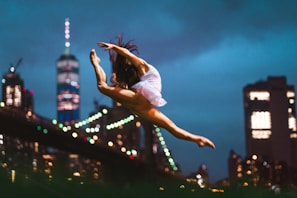 Silhouetted dancer leaping gracefully with a backdrop of urban architecture at twilight