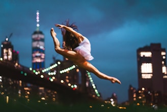 Silhouetted dancer leaping gracefully with a backdrop of urban architecture at twilight