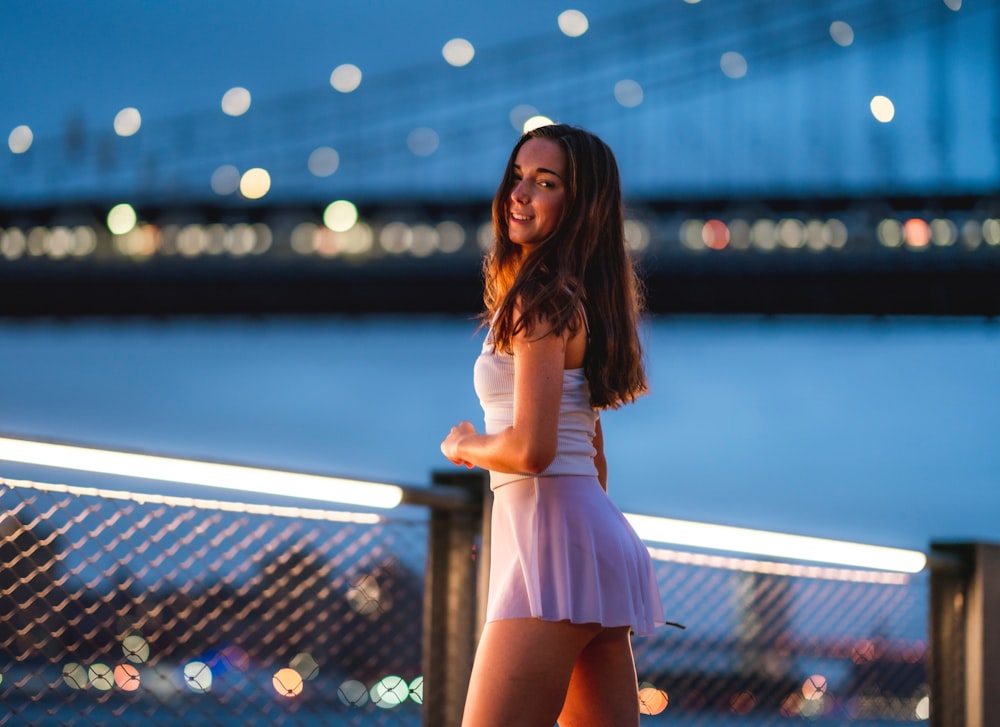 smiling woman in white top and pink skirt by rail near bridge