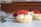 Several small tartlets topped with whipped cream and sliced strawberries are arranged on a marble surface. A whole strawberry and a fork are visible in the background, adding to the delicious and elegant presentation.