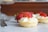 Several small tartlets topped with whipped cream and sliced strawberries are arranged on a marble surface. A whole strawberry and a fork are visible in the background, adding to the delicious and elegant presentation.