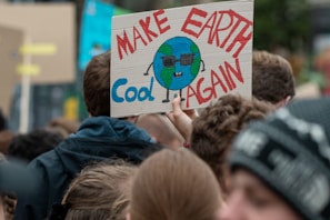 A bold, colorful illustration of a protest sign that reads 'Make Satire Great Again' held by a crowd.