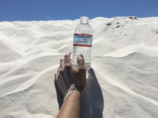 A close-up of an athlete’s hands holding a sleek hydration bottle against a warm sand background.